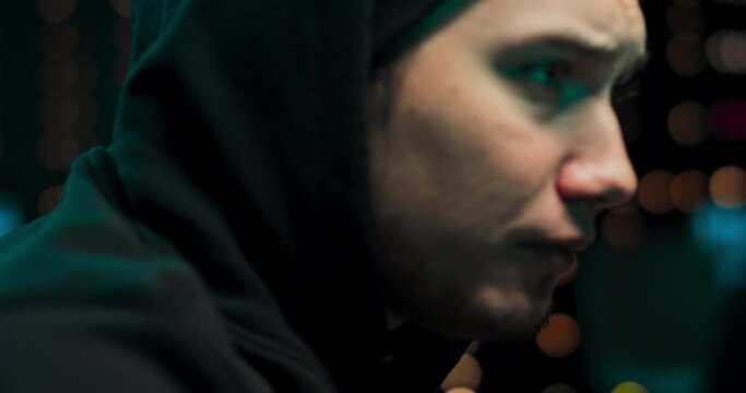 Portrait of hacker wearing a hoodie tries to hack a security system to steal or destroy critical information or a ransom of important information. A teenage hacker eats pizza while writing malware.