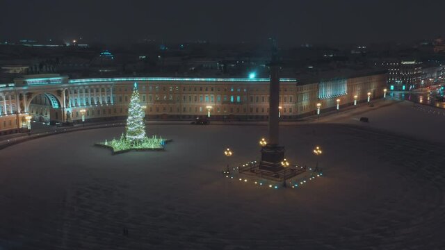 New Year's Palace Square in St. Petersburg. On the square there is a Christmas tree with lights and garlands. Snowfall, night, no people. Cars remove snow. Footage from a quadcopter. View from above.