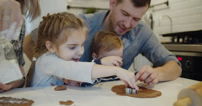 Young family spending time at home together. Parents have fun with children baking christmas cookies pastry in the kitchen. Mother and father teach their daughter and son to use cookie cutters.