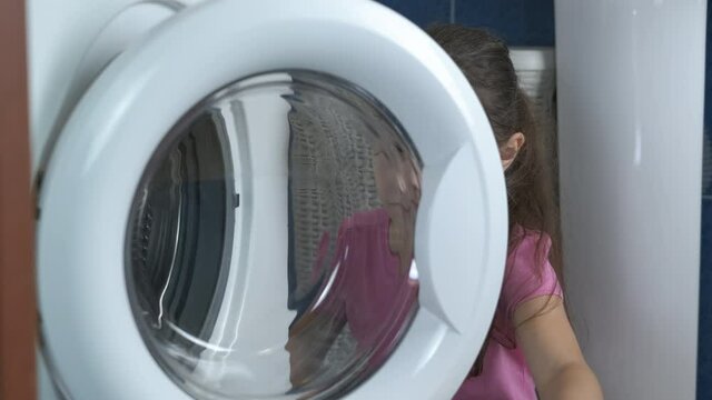 Child housework with washing machine. Cute little girl puts toys in the washing machine.
