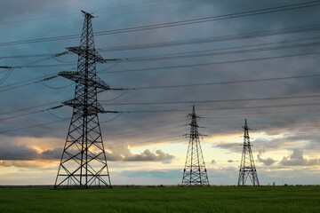 High voltage lines and power pylons in a flat and green agricultural landscape on a sunny day with clouds in the blue sky. Cloudy and rainy. Wheat is growing