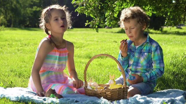 Two children boy and girl having fun and eating chocolate eggs after easter egg hunt in garden backyard