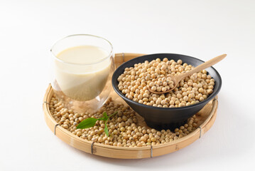 Soybeans seed in a black bowl with spoon and soy milk in a glass on bamboo tray with white background