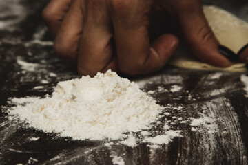 The concept of home baking with raw dough and minced meat, women's hands make cheburek rolled out with a rolling pin, cooking on a wooden background and white flour.