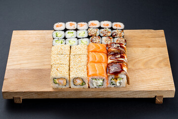 Big sushi set on light wooden dish isolated on black background