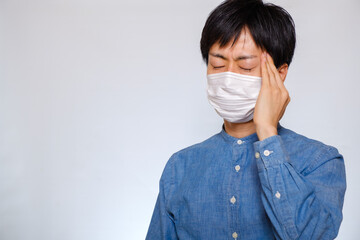 マスクをして頭を押さえる男性　風邪　偏頭痛