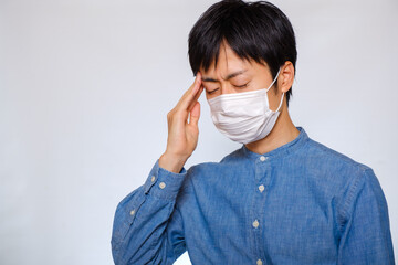 マスクをして頭を押さえる男性　風邪　偏頭痛