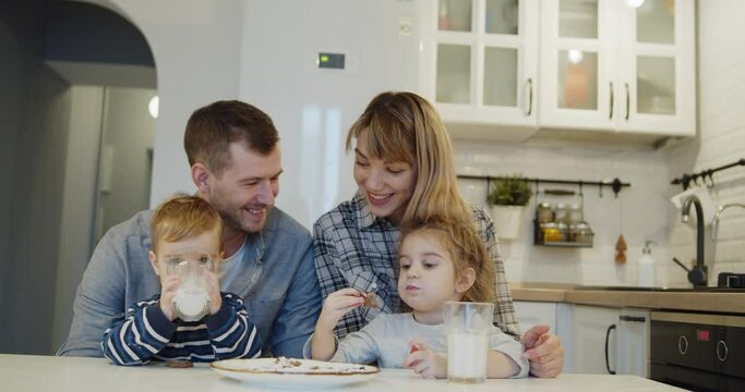 Young family spending time at home together. Parents with children eating traditional homemade gingerbread christmas cookies pastry in the kitchen. Cute kids eat biscuits with milk.