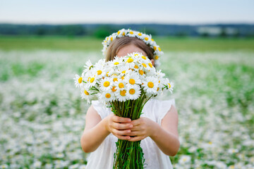 Selective focus. Cute girl with a bouquet of chamomile flowers and a wreath of daisies on her head...