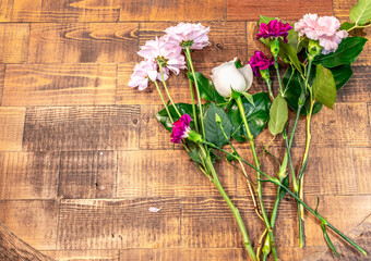 Beautiful long stem blossom flowers with fresh green leaves lay on wooden table surface. Preparation for arranging white rose and colorful florals on a special day. Top view. Happy and romance concept