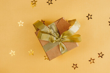 Flat Lay Christmas or Party Background with craft gift box with gold bow on golden background.