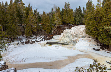 Small frozen waterfall and river covered with snowdrifts