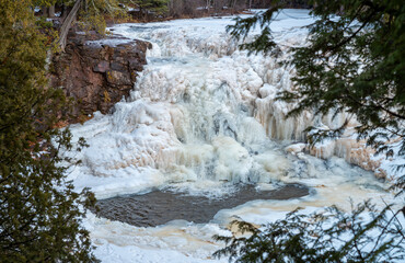 Small frozen waterfall and river covered with snowdrifts
