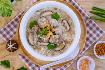 Pork boiled rice with shiitake mushrooms on a white bowl with a spoon placed on a wooden table for breakfast.