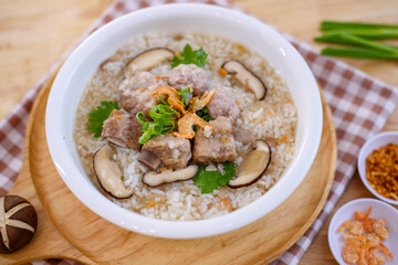 Pork boiled rice with shiitake mushrooms on a white bowl with a spoon placed on a wooden table for breakfast.
