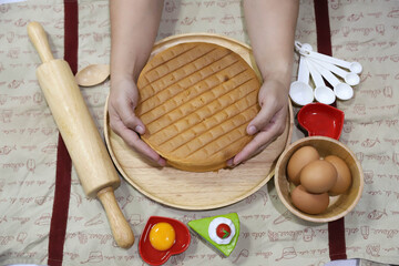 A young woman is taking the cake that is already baked on a wooden tray.