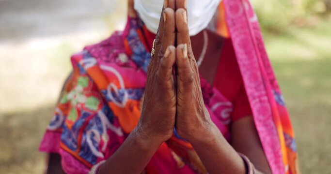 Handheld slow-motion portrait of an elderly women speaks to looking at camera pov wearing face mask to request in prayer position joining hands for Namaste with sign gestures, outdoors