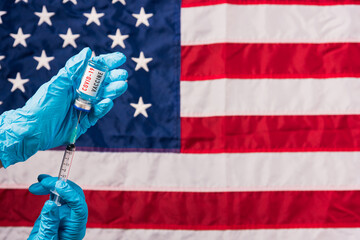 Hands of doctor wear gloves holding coronavirus (COVID-19) vial vaccine and syringe on flag United States of America background, USA Vaccination