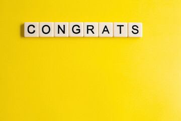 the words congrats written as a flat lay in wood scrabble tiles on a plain yellow background