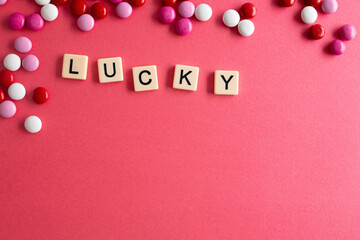 the words lucky written as a flat lay in wood scrabble tiles on a plain red background surrounded by red, white, and pink candies