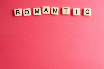 Fototapeta na wymiar the word romantic written as a flat lay in wood scrabble tiles on a plain red background surrounded by red, white, and pink candies