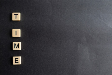 the words time written as a flat lay in wood scrabble tiles on a plain black background