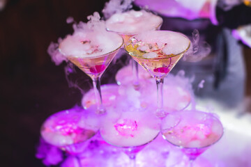 Glasses with alcoholic beverages in the pyramid, filling and pouring beautiful pyramid line of different colored alcohol cocktails with champagne on a party, catering banquet table