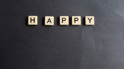 the words happy written as a flat lay in wood scrabble tiles on a plain black background