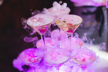 Glasses with alcoholic beverages in the pyramid, filling and pouring beautiful pyramid line of different colored alcohol cocktails with champagne on a party, catering banquet table