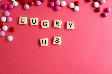 the words lucky you written as a flat lay in wood scrabble tiles on a plain red background surrounded by red, white, and pink candies