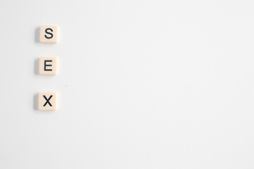 the word sex written as a flat lay in wood scrabble tiles on a plain white background