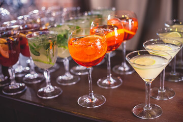 View of alcohol setting on catering banquet table, row line of different colored alcohol cocktails on a party, martini, vodka, spritz and others on decorated catering table event