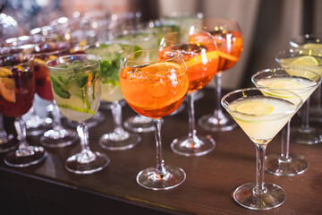 View of alcohol setting on catering banquet table, row line of different colored alcohol cocktails on a party, martini, vodka, spritz and others on decorated catering table event