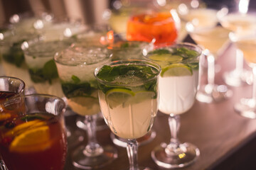 View of alcohol setting on catering banquet table, row line of different colored alcohol cocktails on a party, martini, vodka, spritz and others on decorated catering table event