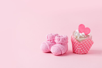 Obraz na płótnie Canvas Cute newborn baby girl shoes with festive decoration cupcake over pink background. Baby shower, birthday, invitation or greeting card idea, copy space, flyer, invitation, monochrome concept