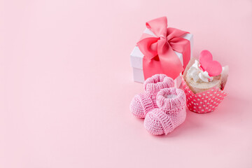 Cute newborn baby girl shoes with festive decoration cupcake and gift box  over pink background. Baby shower, birthday, invitation or greeting card idea, copy space, flyer, invitation, monochrome