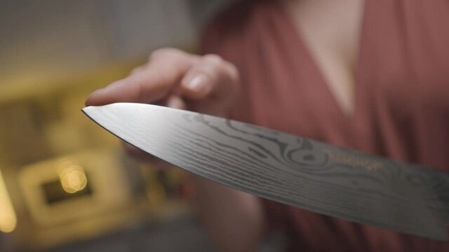 Close-up of woman holding sharp knife. Action. Woman checks sharpness of knife at tip before slicing. Woman intimidatingly holds knife before cooking in kitchen