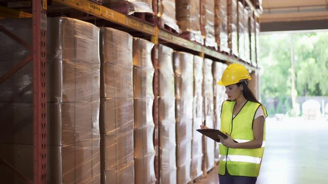 Female Warehouse Worker Wearing Hard Hats Walking And Checks Goods Inventory Stock On Goods Shelf In Distribution Fulfillment Center. ECommerce Business And Freight Transportation Logistic Concept.