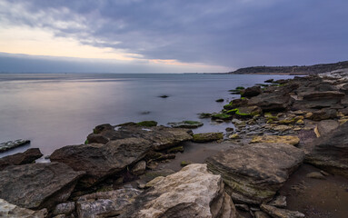Fototapeta na wymiar Cloudy sunrise on rocky sea coast, long exposure