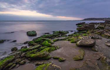Fototapeta na wymiar Cloudy sunrise on rocky sea coast, long exposure