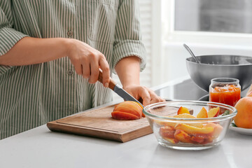 Woman cutting peaches for preparing tasty jam