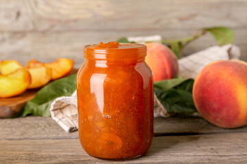 Jar with tasty peach jam on wooden table