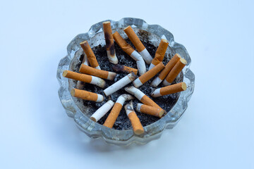 Cigarette butts in glass ashtray on white background.
