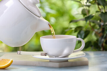 Pouring tea from teapot in cup on table against blurred background