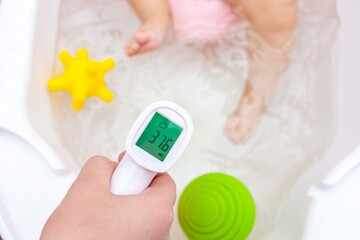 Woman's hand with an infrared thermometer measures the temperature of the water in the baby's bath
