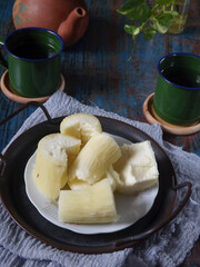 Steamed cassava or singkong rebus is traditional and modest snack in Indonesia. Commonly served with coffee or tea for breakfast or snacking time. Enamel cups and clay tea pot also appeared in frame. 