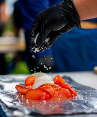Mano con guante de látex negro . agregando sal a mezcla de jitomate y cebolla sobre papel...