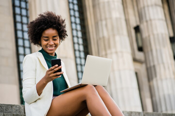 Business woman talking on phone and using laptop outdoors.