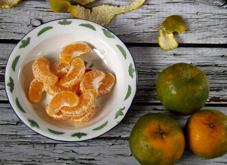 Image of the whole and peeled of jeruk keprok or Indonesian local orange fruits which commonly has green with bit yellow skin. The taste is very refreshing, sweet with bit sour. High angle picture.