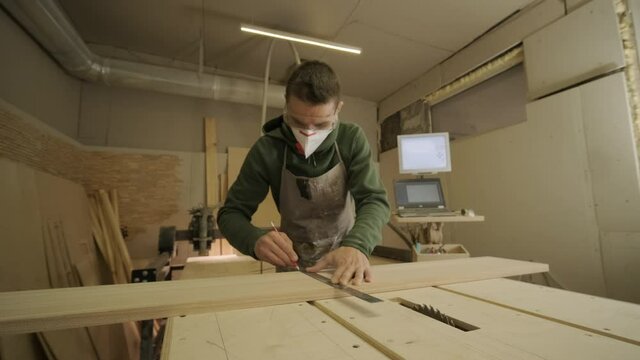 Hardworking professional carpenter in mask and glasses holding a ruler